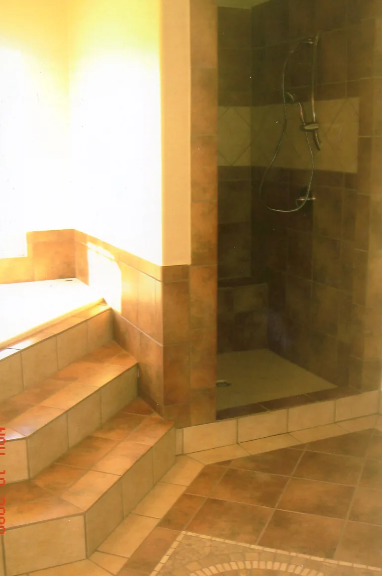 Custom bathroom remodel with beige tiled walk-in shower, built-in corner shelves, and tiled steps leading to the shower area, showcasing a modern and accessible design.