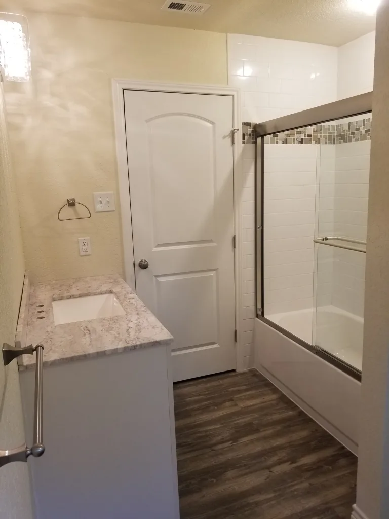 Contemporary bathroom with wood-look flooring, white subway tile shower with mosaic accent, and a sleek vanity with marble countertop and towel holder.