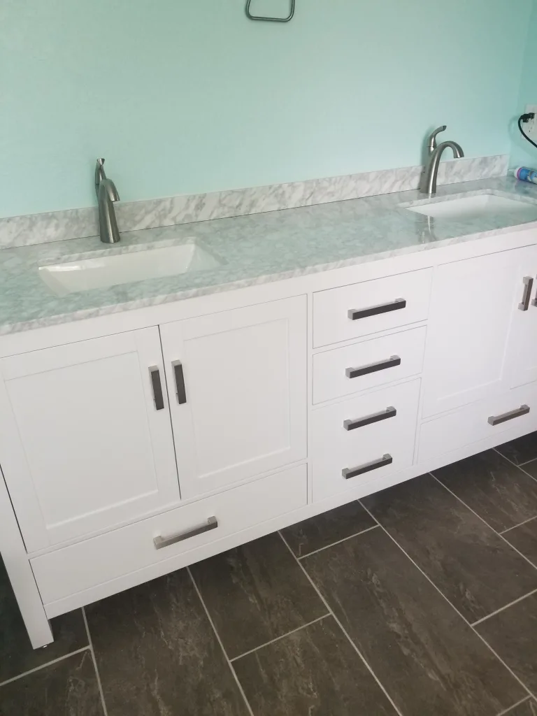 Fresh bathroom with a white modern double vanity, marble countertop, and rectangular undermount sinks against a turquoise wall, paired with dark tiled flooring.