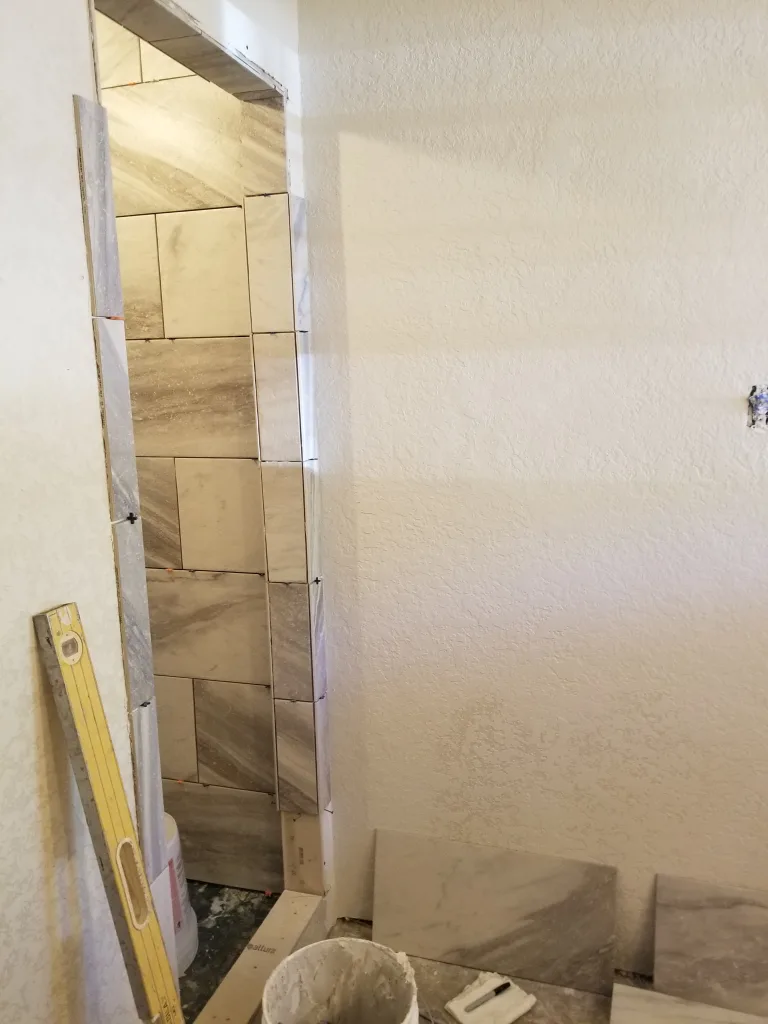 In-progress bathroom wall tiling with large marble tiles and tools, showing the renovation and installation process for a modern bathroom design.