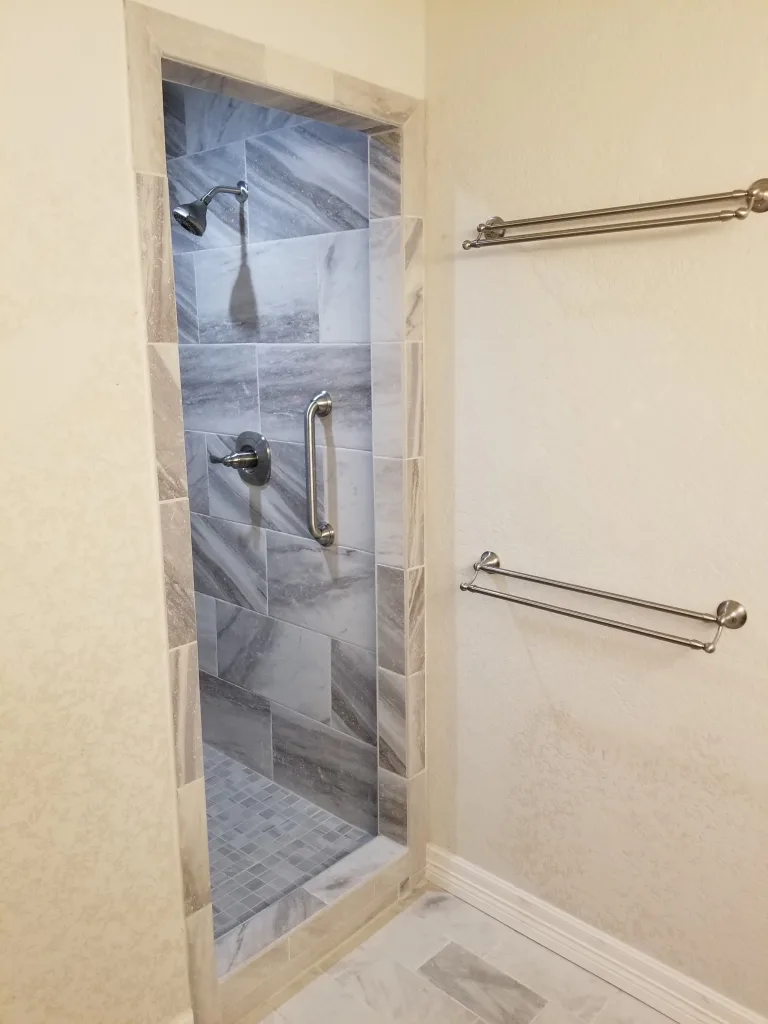 Elegant and modern shower design with vertical marble tiles, a square tile floor, brushed nickel fixtures, and safety grab bars for accessibility.