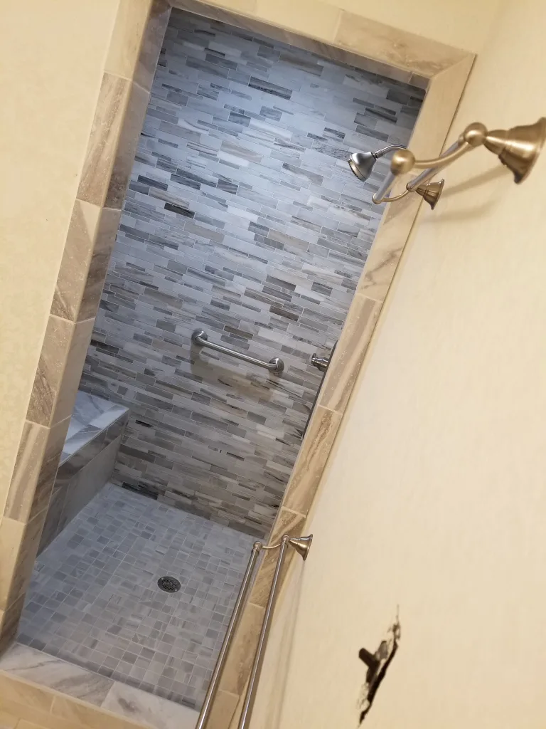 Stylish shower with an array of gray tone mosaic tiles, a built-in niche, and modern brushed nickel shower fixtures, viewed past a sleek glass shower door.