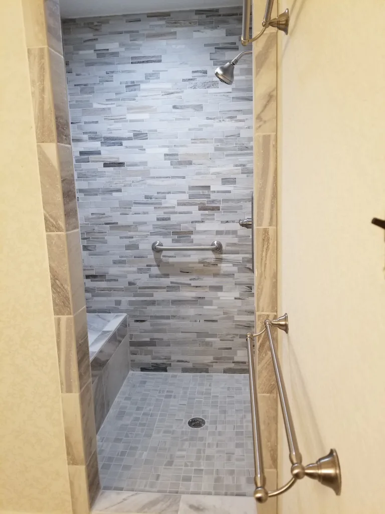 Modern walk-in shower with mixed gray mosaic tile walls, a built-in bench, and brushed nickel fixtures, complemented by a herringbone tile floor.