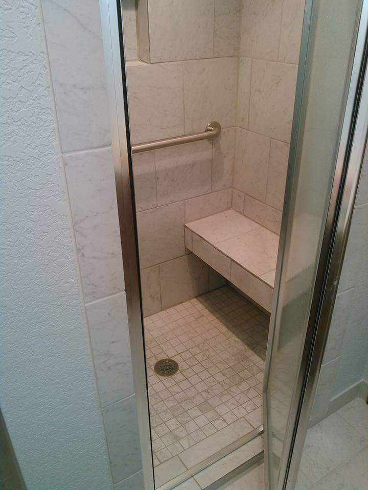 Modern shower enclosure with marble tile, built-in corner seat, and a silver safety grab bar, showcasing a sleek and accessible design.