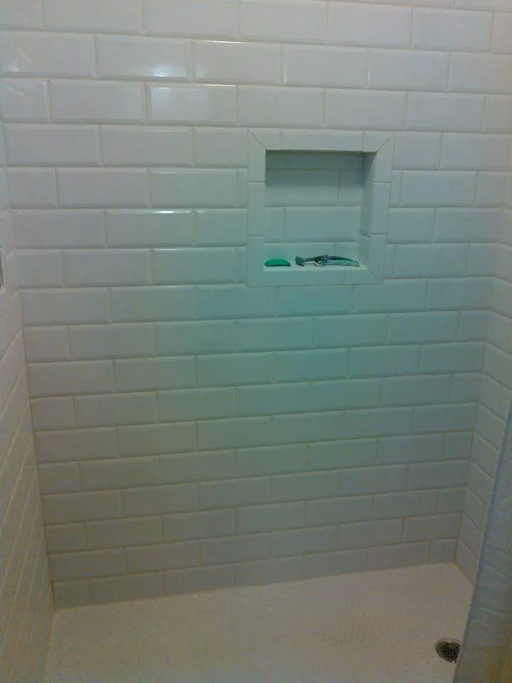 Clean and modern shower corner with glossy white subway tiles and a built-in niche for toiletries, showcasing a simple and contemporary bathroom design.